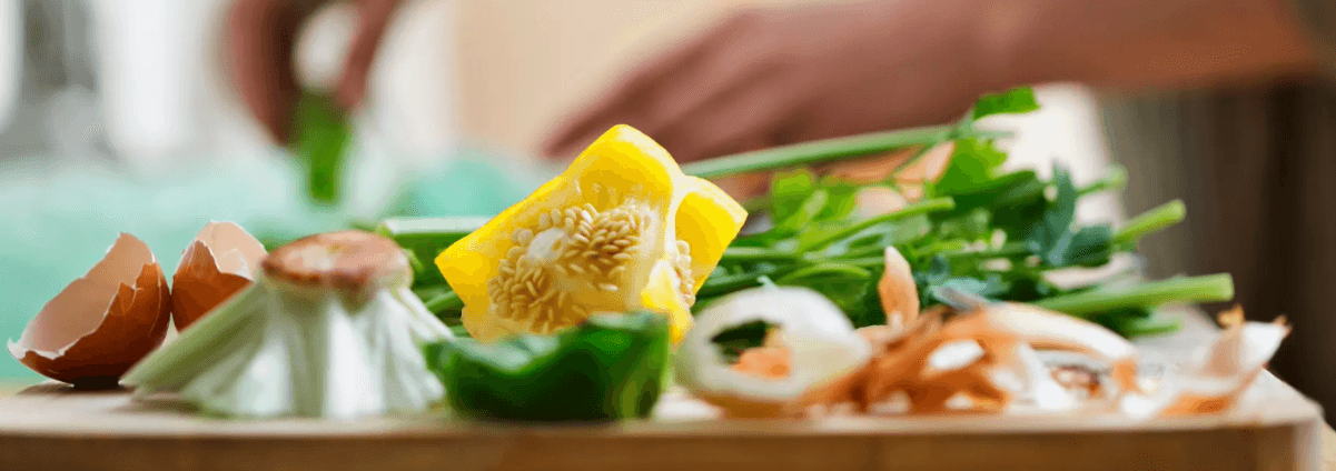 A chopping board with egg shells, inedible parts of a yellow pepper, top of a lettuce and onion skin